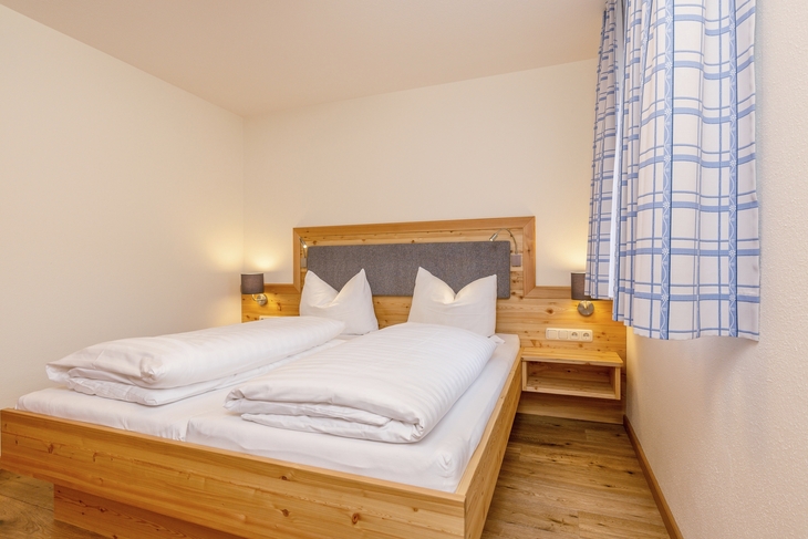 Holzbett mit weißer Bettwäsche in einem gemütlichen Schlafzimmer.