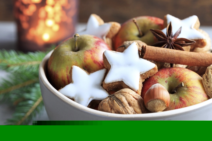 Schale mit Weihnachtsgebäck, Äpfeln, Nüssen und Zimtstangen.