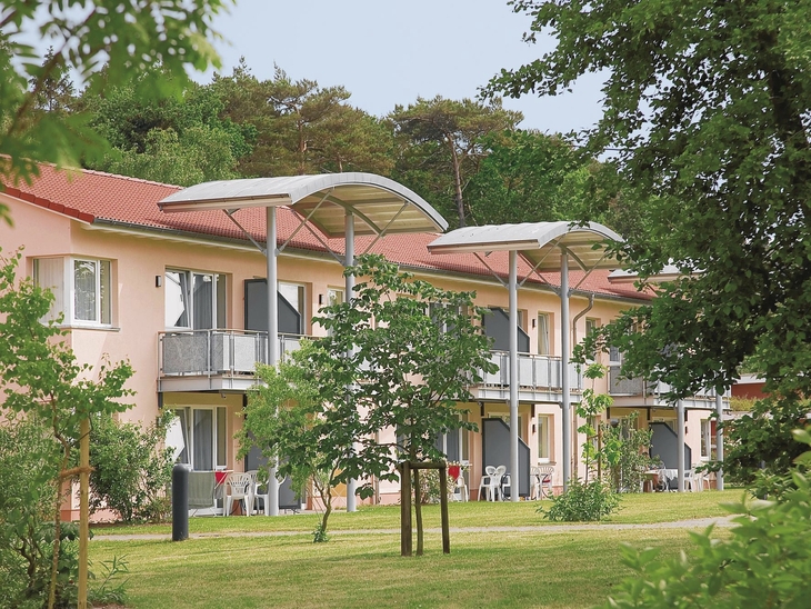 Außenansicht einer Ferienanlage mit Balkonen und grüner Umgebung.