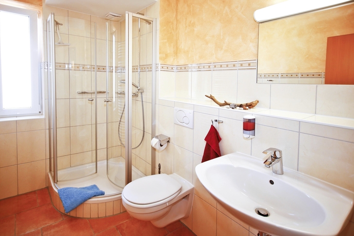 Helles Badezimmer mit Dusche, WC und Waschbecken in einer Ferienanlage.