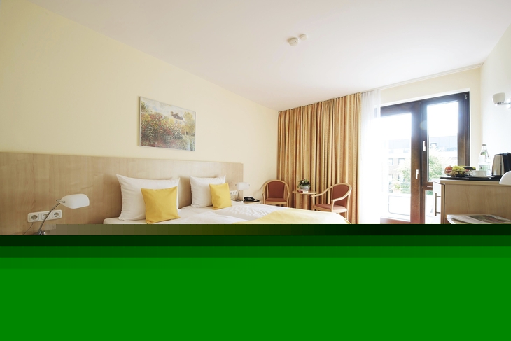 Helles Zimmer mit rotem Teppichboden im Haus Oldenburg in der Ferienanlage Timmendorfer Strand. Doppelbett mit gelber Bettwäsche, Nachtischen und zwei Stühlen mit kleinem Tisch, sowie einem Schreibtisch und Balkontür mit großem gelb-rotem Vorhang.