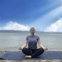 Person meditiert im Lotussitz auf einer Yogamatte am Ufer eines Sees.