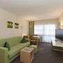 Wohnzimmer mit grüner Couch, Esstisch und Flachbildfernseher.
