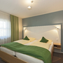 Hotelzimmer mit Doppelbett, grüner Bettdecke und hellem Holzmobiliar.