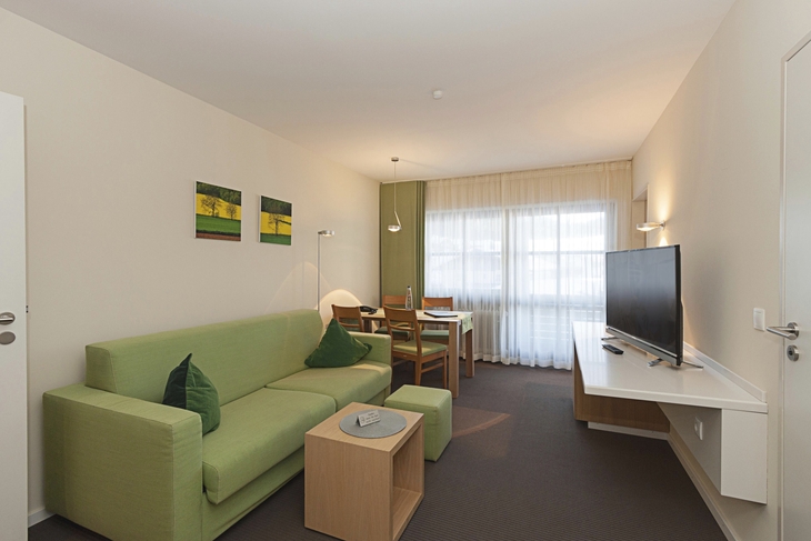 Wohnzimmer mit grüner Couch, Esstisch und Flachbildfernseher.