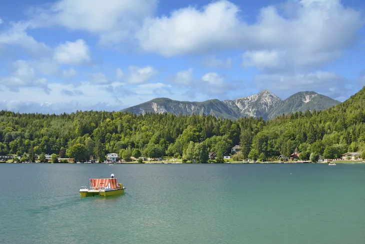 Pedalboot auf dem Klopeiner See vor bewaldeten Bergen und blauem Himmel.