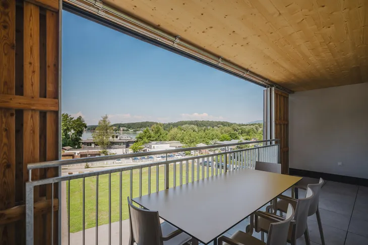 Blick von einer überdachten Terrasse auf eine grüne Landschaft und Häuser in der Ferne.