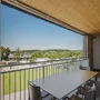 Blick von einer überdachten Terrasse auf eine grüne Landschaft und Häuser in der Ferne.