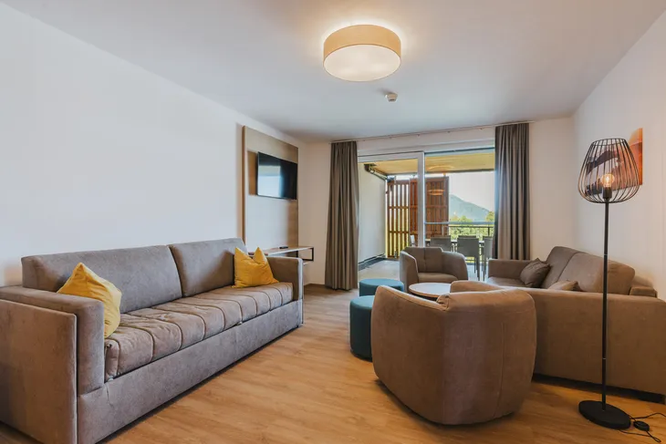 Modernes Wohnzimmer mit Sofa, Sesseln und Blick auf einen Balkon.