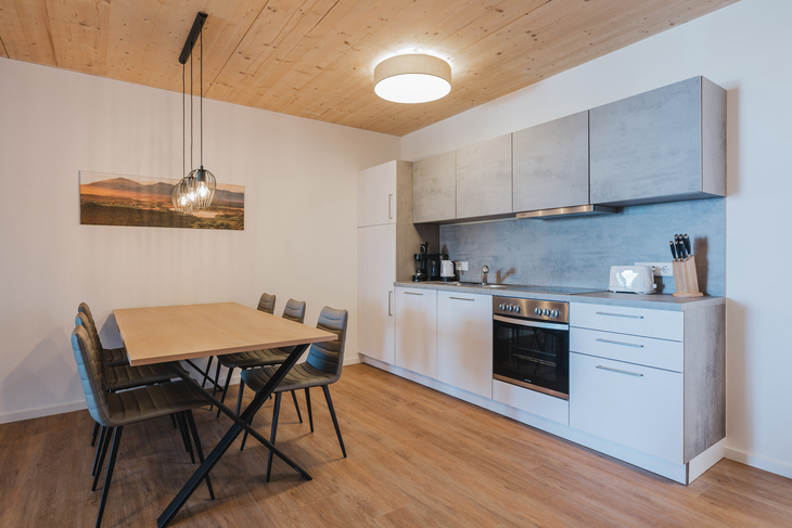 Moderne Küche mit Esstisch, Hängelampen und Einbaugeräten in Holzoptik.