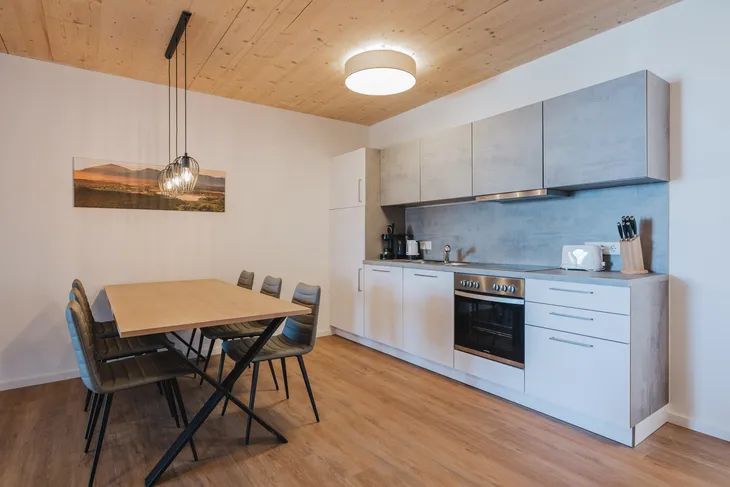 Moderne Küche mit Esstisch, Hängelampen und Einbaugeräten in Holzoptik.