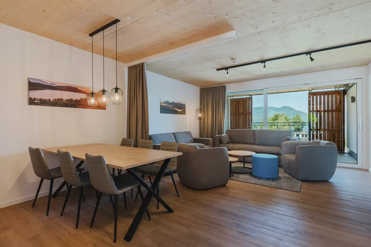 Wohnbereich mit Esstisch, Sofas, Holzdecke und offenem Balkon mit Bergblick.