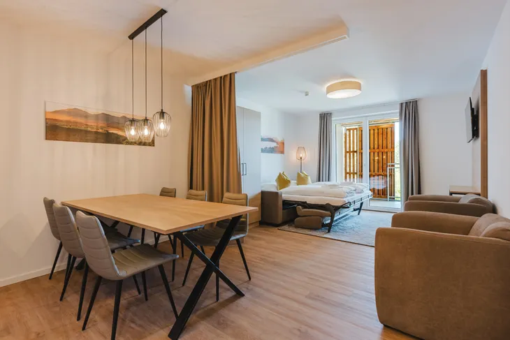 Wohnbereich mit Esstisch, Sofa, Bett und Balkon im modernen Stil.