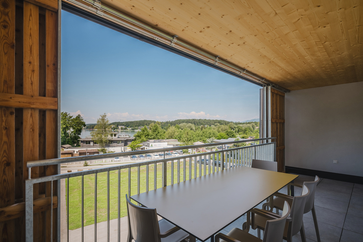 Blick von einer überdachten Terrasse auf eine grüne Landschaft und Häuser in der Ferne.