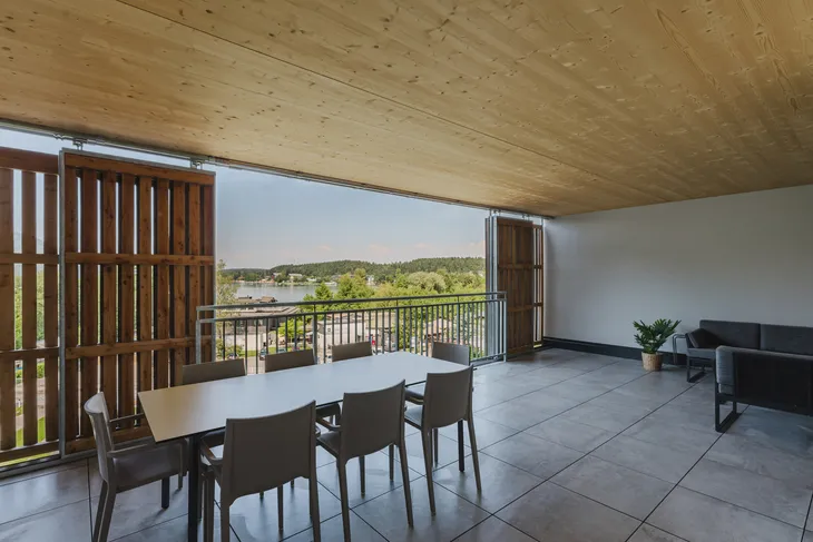 Überdachte Terrasse mit Tisch, Stühlen und Ausblick auf einen See.