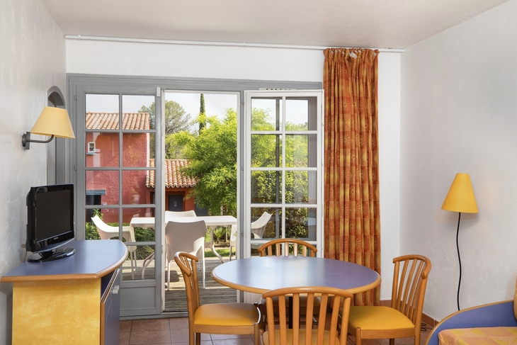 Wohnzimmer mit Tisch, Stühlen und Blick auf eine Terrasse durch große Fenster.
