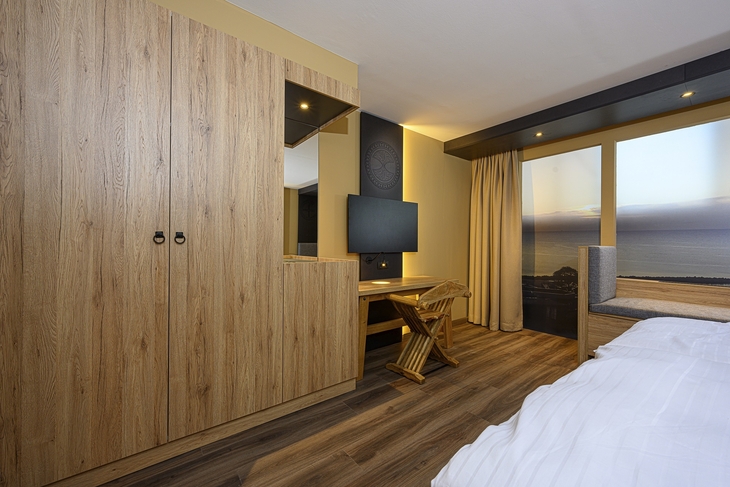 Hotelzimmer mit Holzinterieur, Schreibtisch, Fernseher und Meerblick.