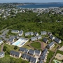 Luftaufnahme einer Ferienanlage mit Pool, grüner Umgebung und Blick auf das Meer.