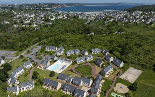 Luftaufnahme einer Ferienanlage mit Pool, grüner Umgebung und Blick auf das Meer.