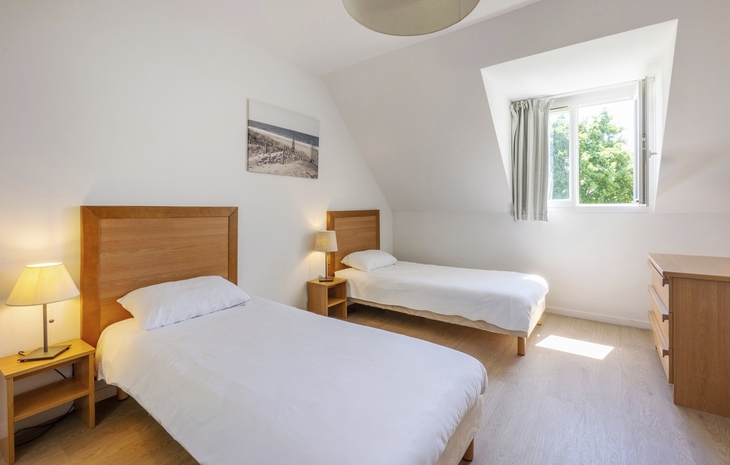 Helles Zimmer mit zwei Einzelbetten, Nachtlampen und einem Fenster.