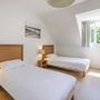 Helles Zimmer mit zwei Einzelbetten, Nachtlampen und einem Fenster.