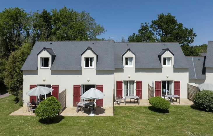 Ferienhäuser mit grauen Dächern und roten Fensterläden, umgeben von Rasen und Bäumen.