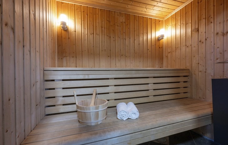 Sauna mit Holzwänden, Bank, Eimer und zwei Handtüchern.