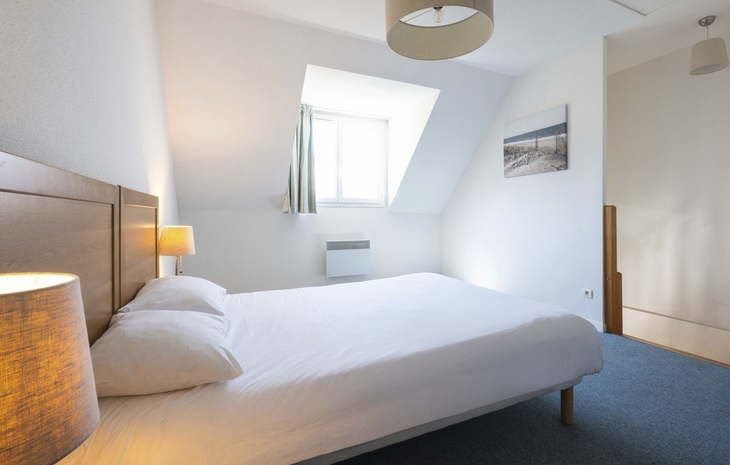 Helles Schlafzimmer mit Doppelbett, Wandlampe und Fenster.