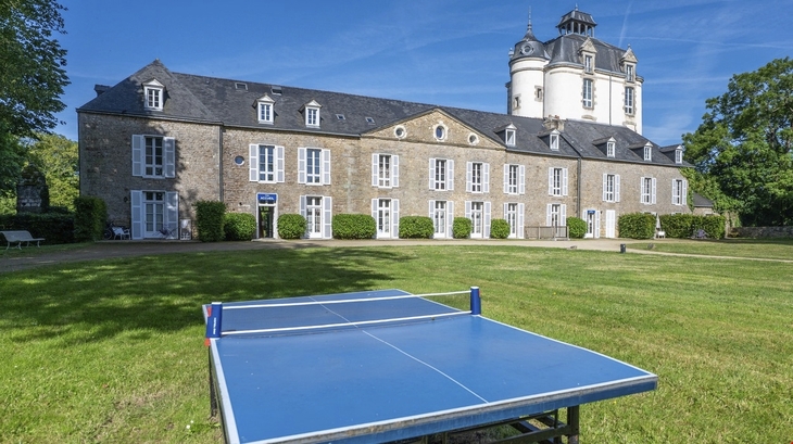 Steinresidenz mit Turm, großer Rasen und Tischtennisplatte im Vordergrund.