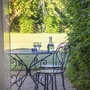 Metalltisch mit zwei Stühlen im Garten mit Blick durch offene Tür.