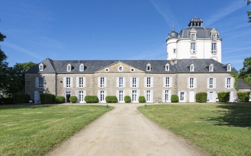 Zufahrtsweg zu einem historischen Schloss mit großem Turm und angrenzender Grünanlage.
