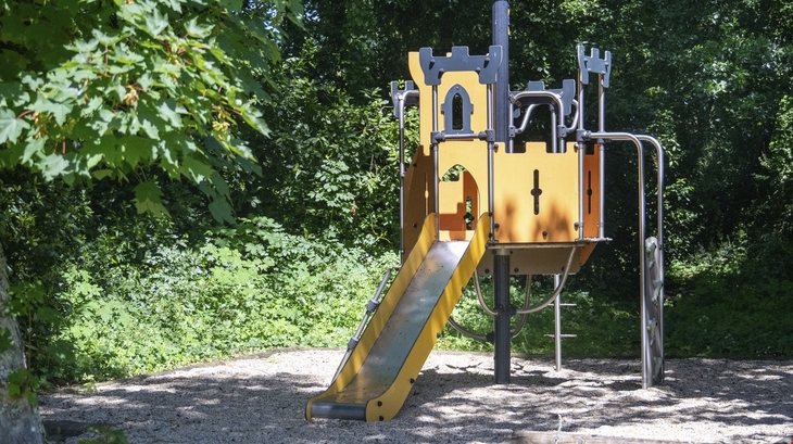 Ein Spielplatz mit einer gelben Rutsche und Klettergerüst im Wald.