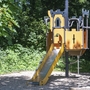 Ein Spielplatz mit einer gelben Rutsche und Klettergerüst im Wald.