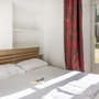 Helles Schlafzimmer mit Doppelbett, roten Vorhängen und Sonnenlicht durch Terrassentür.