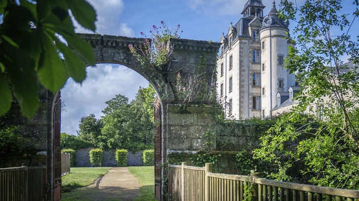 Historisches Schloss mit Torbogen und Gartenansicht.