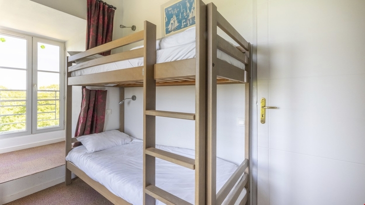 Etagenbett in hellem Raum mit Fenster und rotem Vorhang.