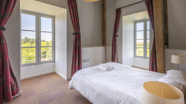 Helles Schlafzimmer mit Doppelbett, roten Vorhängen und Blick ins Freie.