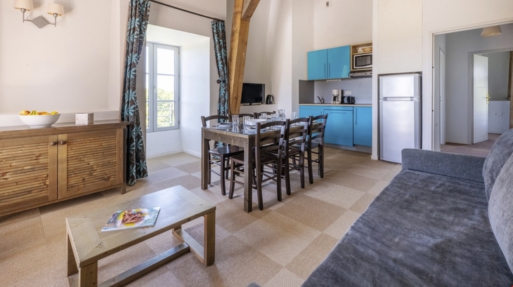 Wohnzimmer mit Esstisch, blauer Küche und Fenster in einem Ferienhaus.