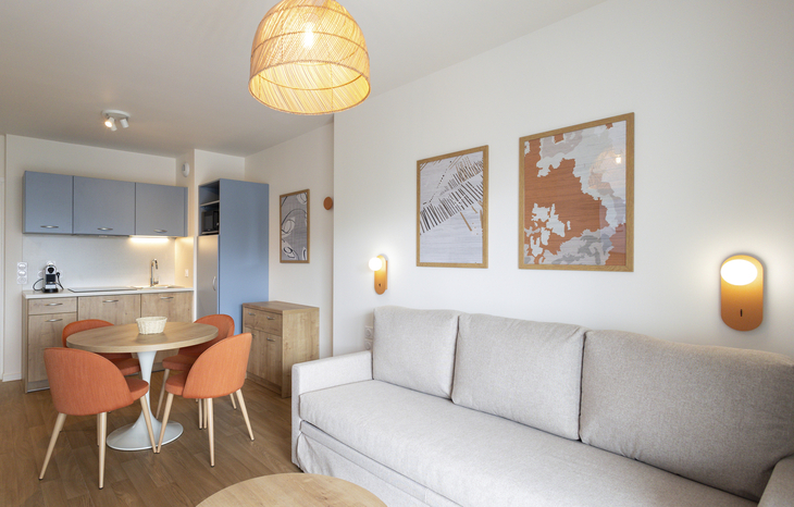 Wohnzimmer mit Sofa, Tisch, Essbereich und Wanddekorationen in moderner Ferienwohnung.