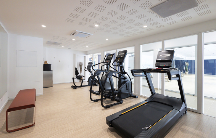 Fitnessraum mit Laufband, Crosstrainer und heller Einrichtung.
