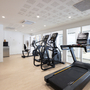Fitnessraum mit Laufband, Crosstrainer und heller Einrichtung.
