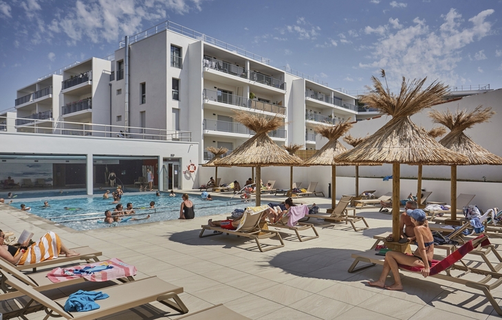 Ein moderner Apartmentkomplex mit einem Außenpool und Sonnenliegen.