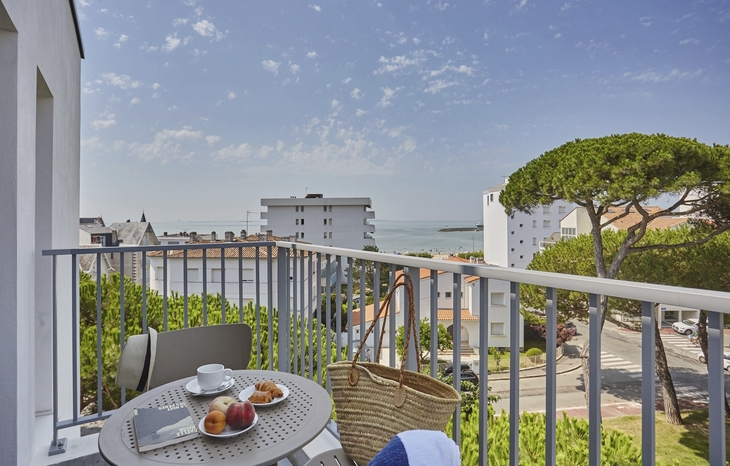 Balkon mit Tisch, Stühlen und Ausblick auf Gebäude und das Meer im Hintergrund.