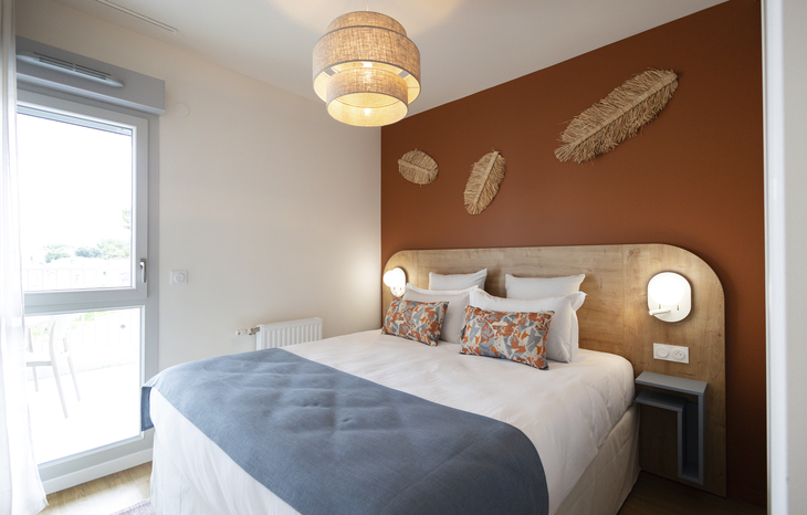 Schlafzimmer mit Doppelbett, Wanddekorationen und großem Fenster.