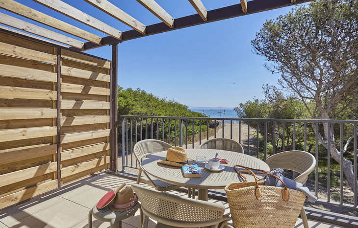 Terrasse mit Esstisch, Stühlen, Blick auf Meer und Bäume.