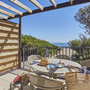 Terrasse mit Esstisch, Stühlen, Blick auf Meer und Bäume.