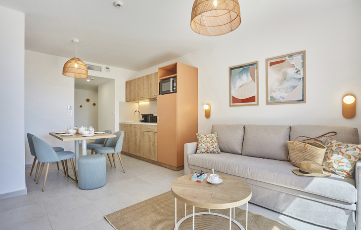Helles Wohnzimmer mit Sofa, Esstisch und Küchenzeile in einer Ferienwohnung.