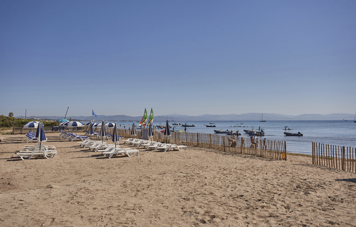 Sonniger Strand mit Liegestühlen und Blick auf das Meer.