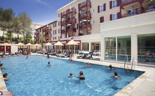 Außenpool einer Ferienresidenz mit Sonnenliegen und Badenden im Wasser.