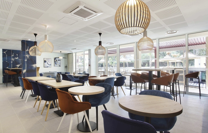 Moderne Café-Lounge mit Holztischen, blauen und braunen Stühlen und großen Fenstern.